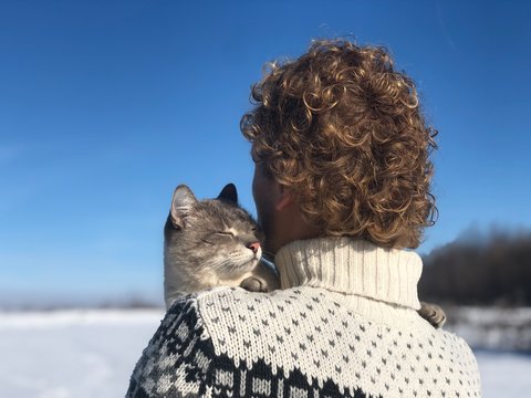 blue-eyed gray-white Siamese cat hugs with love and devotion to his owner - blonde curly-haired guy. The cat was lost outside on a clear Sunny winter day and is now found and happy. The pet hugs owner
