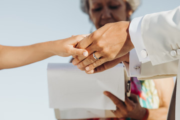 Bride and groom in light summer clothes hold each other hands during the ceremony