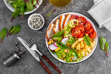 Grilled chicken meat with fresh vegetable salad of tomato, cucumber, radish, lettuce, mangold leaves, corn and pasta for lunch, top view