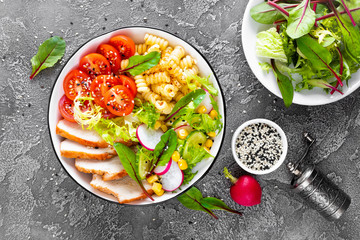 Grilled chicken meat with fresh vegetable salad of tomato, cucumber, radish, lettuce, mangold leaves, corn and pasta for lunch, top view