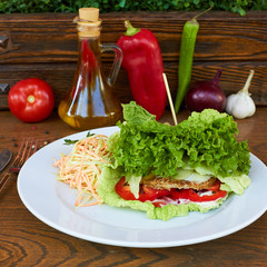  green burger. lettuce, greens, tomatoes, peppers, carrots. healthy food. In the background is a glass bottle of olive oil, green and red peppers, onions, tomato and garlic.