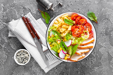 Grilled chicken meat with fresh vegetable salad of tomato, cucumber, radish, lettuce, mangold leaves, corn and pasta for lunch, top view