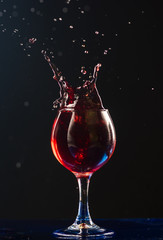 A small glass with wine on a black background and splashes nearby