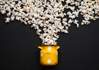 popcorn on a dark background, pouring out of a yellow can with white polka dots