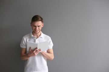 Handsome young man with book on grey background