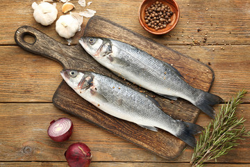 Board with tasty fresh seabass fish on wooden background