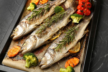 Baking sheet with tasty cooked seabass fish and vegetables on dark table