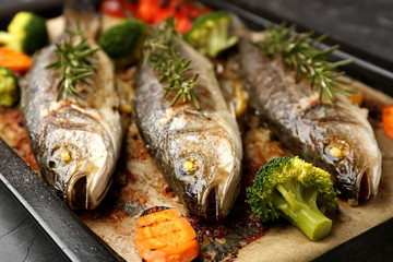 Tasty cooked seabass fish and vegetables on baking sheet