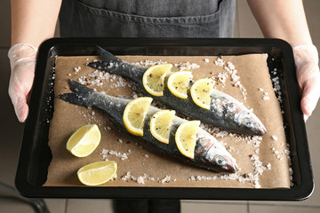 Woman holding baking sheet with raw seabass fish, closeup