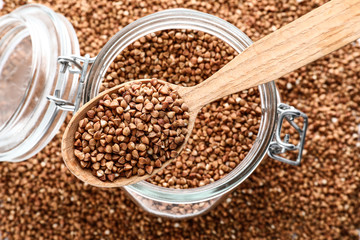 Glass jar and spoon with raw buckwheat, top view