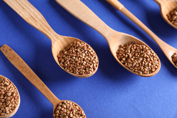 Spoons with raw buckwheat on color background