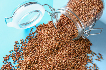 Overturned glass jar with raw buckwheat on color background