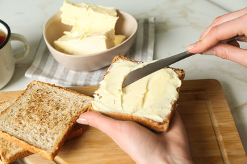 Woman spreading tasty toast with butter at table