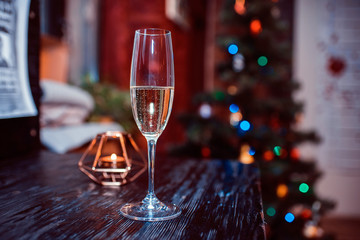 glass with champagne against the background of a candle and a fir-tree. New Year's background