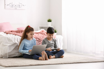 Cute little children with laptop and tablet computer watching cartoons at home