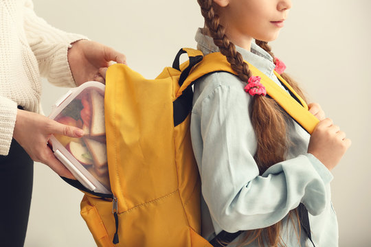 Mother putting lunch box into backpack of her little daughter before school