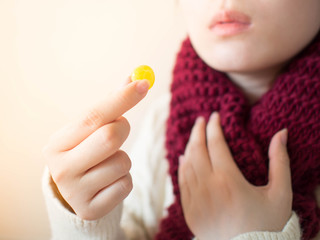 Female taking medical lozenges with honey lemon flavored for relief sore throat, irritating cough and mouth pain. Close up of girl with scarf feeling sick and cold in winter. Health care concept.