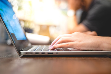 close up image of hand working and typing on laptop, computer keyboard on wood table, at cafe or coffee shop