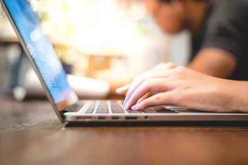 close up image of hand working and typing on laptop, computer keyboard on wood table, at cafe or coffee shop