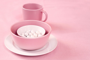 Pink and white crockery with sugar dragees inside on a pink cloth background