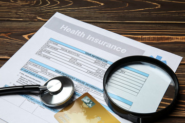 Health insurance form with magnifier, credit card and stethoscope on wooden table