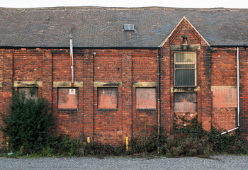 An old abandoned brick factory building with boarded up windows and crumbling decaying walls...