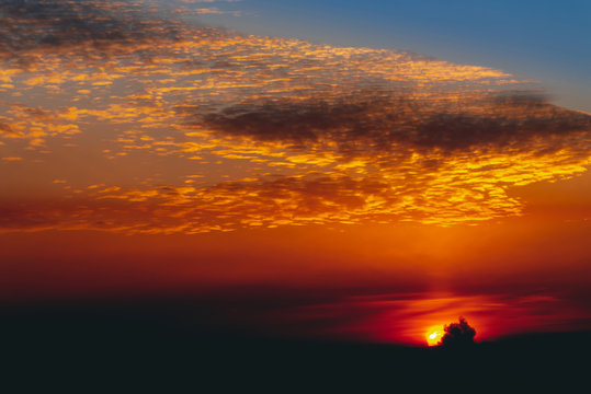 Sunny shine on clouds. Wonderful vivid dawn. Beautiful calm orange sunset. Scenic surreal sunrise. Amazing red blue cloudy sky. Picturesque sundown. Atmospheric cloudscape. Circle of sun above horizon © Daniil