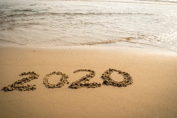 Happy New Year 2020 concept, 2020 number lettering on the sea beach, wave and golden light of sunset.