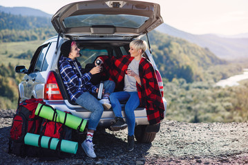 Traveling, tourism and friendship concept. Young friends travelers sitting on trunk of car and...
