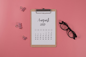 Flat lay calendar with clipboard and glasses on pink background. August 2019. top view.