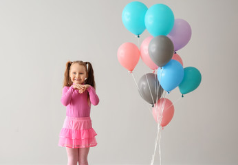 Cute little girl with balloons near white wall