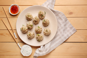Plate with tasty dumplings and sauces on wooden table