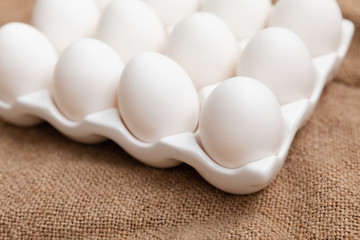 White Chicken Eggs In Ceramic Carton Holder On Burlap Background