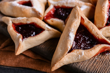 Tasty hamantaschen for Purim holiday on wooden board, closeup