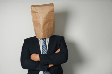 Businessman with paper bag on his head against light background