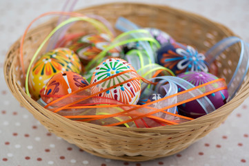 Fototapeta na wymiar Colorful painted Easter eggs in brown wicker basket covered with colorful ribbons, traditional Easter still life