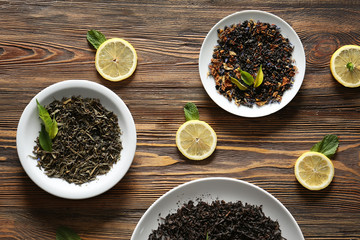 Plates with different types of dry tea leaves and lemon slices on wooden table