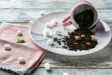 Overturned cup with dry tea leaves and sugar on plate