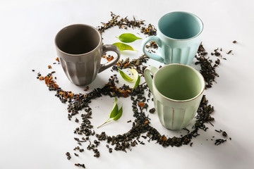 Composition with empty cups and different types of dry tea leaves on white background