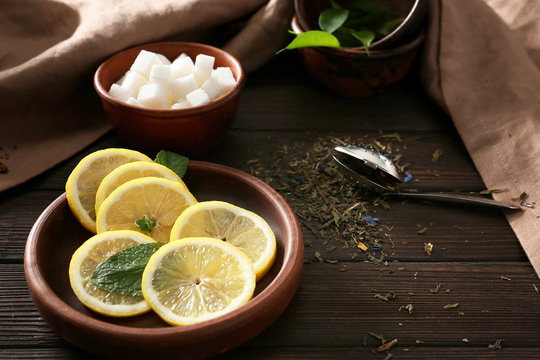 Dry Tea Leaves, Bowl With Lemon Slices And Sugar On Wooden Table