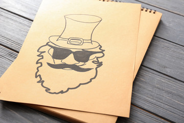 Paper with drawing of leprechaun on wooden table. St. Patrick's Day celebration