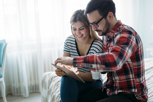Young happy couple using tablet in bedroom