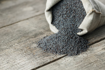 Poppy seeds in a burlap bag on a vintage wooden gray background. The tasty and useful seeds rich with protein and oils.