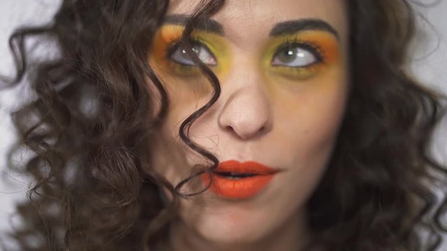 Close up portrait of smiling young curly beautiful girl with bright make up blowing off curl. Slow motion.