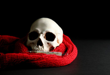 Human skull, scarf and thermometer on dark background