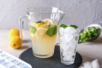 Jug of fresh lemonade and glass with ice on table