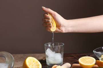Woman squeezing lemon juice into glass with ice on table
