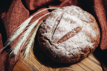 Fresh brown bread with spikelets on wooden background