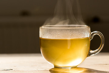 Steaming hot tea in glass mug on a wooden table. Refreshing morning image with a tea cup in back...