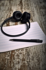 Composition of black headphones next to an empty pentagram notebook